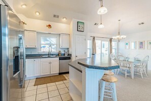 A modern kitchen with white cabinets, a stainless steel refrigerator, a large island with stools, and a dining area with white chairs.
