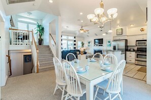 A spacious kitchen with modern appliances, a dining area with white chairs, and a staircase leading to a loft.