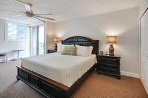 A bedroom with a large bed, two bedside tables with lamps, a ceiling fan, and a view of the outdoors through a window with blinds. - Trillium 5C - Premier (Madeira Beach)