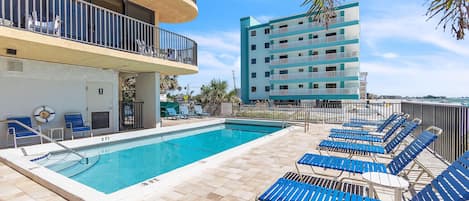 Une piscine avec des chaises longues et un bâtiment doté de balcons.