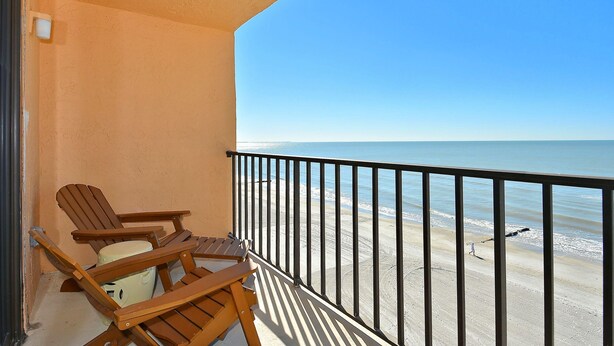 A balcony with wooden chairs and a view of the beach.