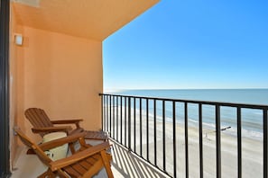 Un balcon avec des chaises en bois et vue sur la plage.