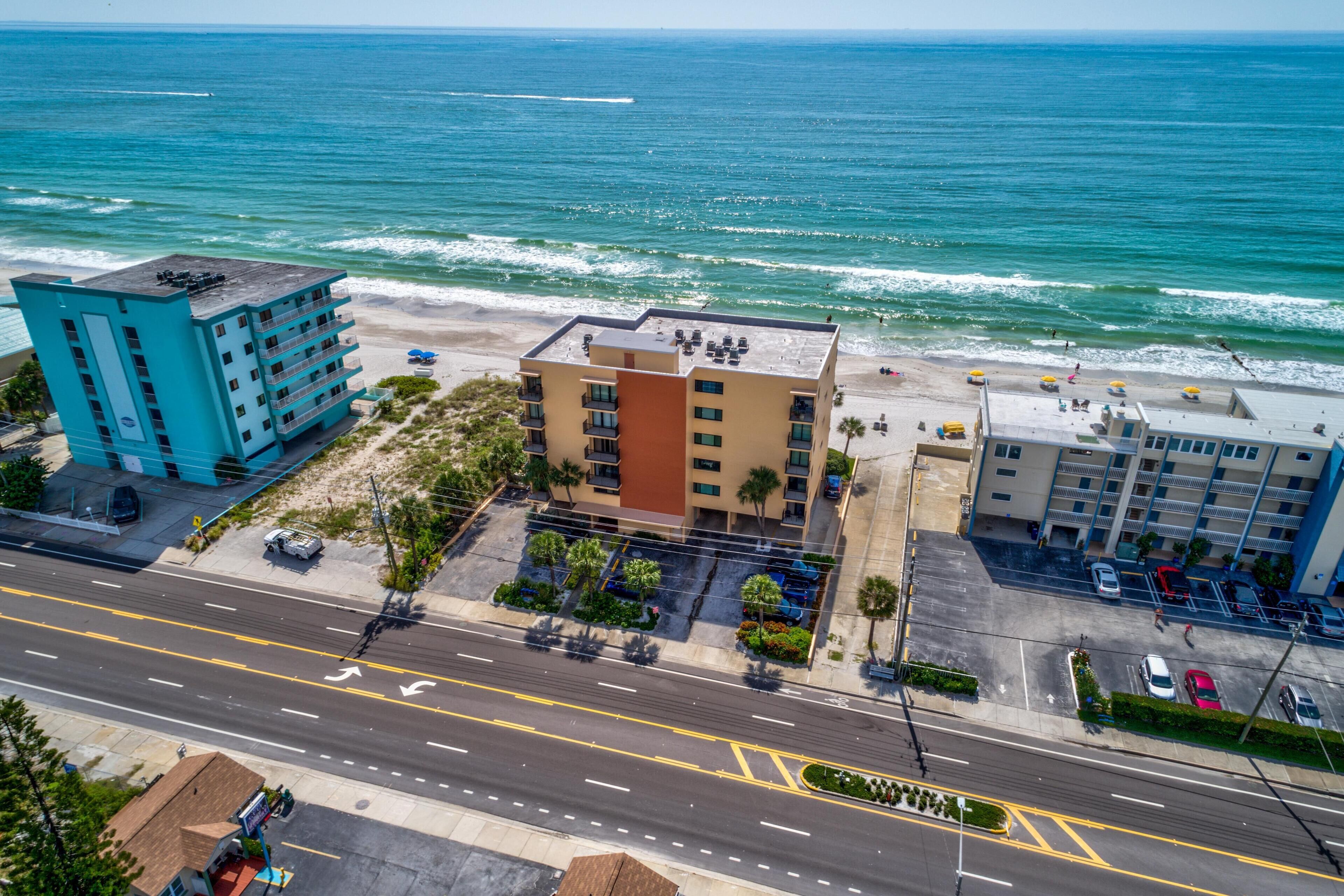 A coastal hotel with a view of the ocean, a parking lot, and a road with directional arrows.