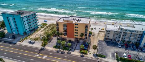 A coastal hotel with a view of the ocean, a parking lot, and a road with directional arrows.