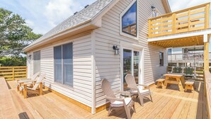 Ein zweistöckiges Haus mit einer Holzterrasse, Sitzgelegenheiten im Freien und einem überdachten Bereich.