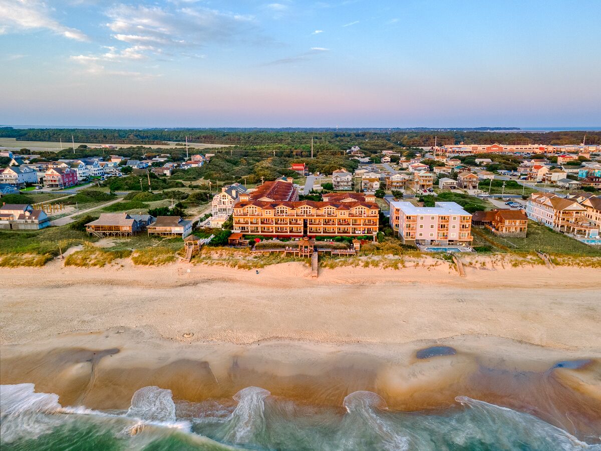 A coastal town with a large hotel featuring multiple floors and balconies, situated near a sandy beach.