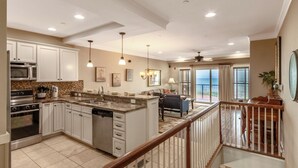 A spacious kitchen with white cabinets, a central island, and a dining area with a view. - Luxury oceanfront condo with community indoor & outdoor pools, hot tub & more (Kill Devil Hills)