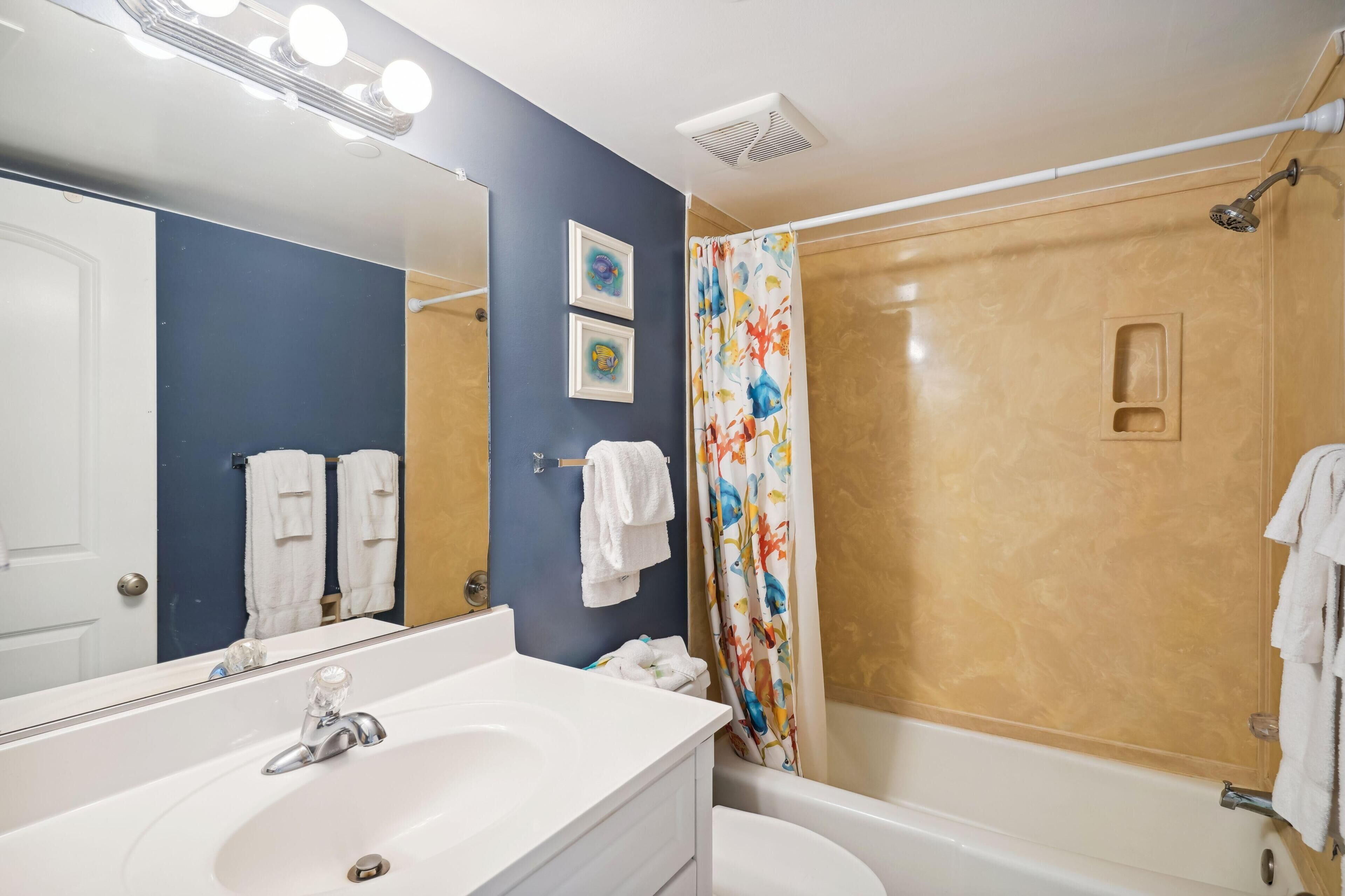 Une salle de bain avec un lavabo blanc, un miroir, une douche avec un rideau coloré et un mur beige.