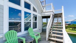 A wooden deck with two green Adirondack chairs, a wooden table, and a staircase leading to a deck area. - Spacious pet-friendly home on Hatteras Island w/ a private pool & hot tub! (Avon)
