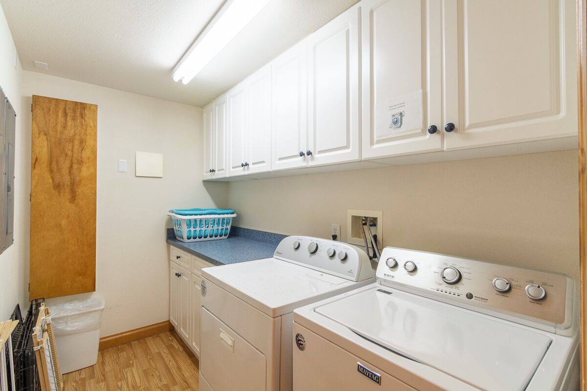 A laundry room with two white washers and dryers, a blue laundry basket, and white cabinets.