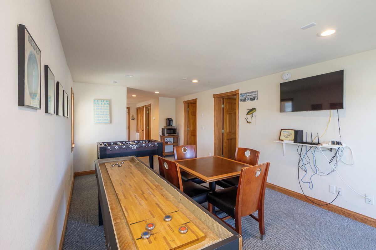 A room with a foosball table, a pool table, a television mounted on the wall, and a sign on the door.