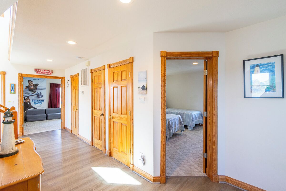 A hallway with wooden doors, a framed picture on the wall, and a bed in the adjacent room.