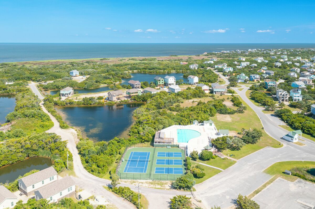 An aerial view of a residential area with houses, a tennis court, and a large body of water.