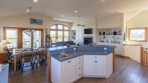 A spacious kitchen with a large island, white cabinetry, and a dining area with chairs. - Spacious pet-friendly home on Hatteras Island w/ a private pool & hot tub! (Avon)