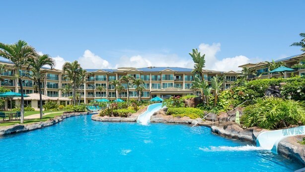 A resort pool with a water slide, palm trees, and a building with multiple balconies.