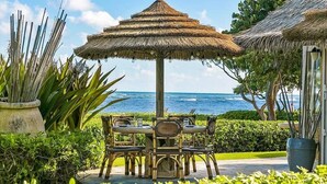 An outdoor dining area with a thatched umbrella, wicker chairs, and a view of the ocean.