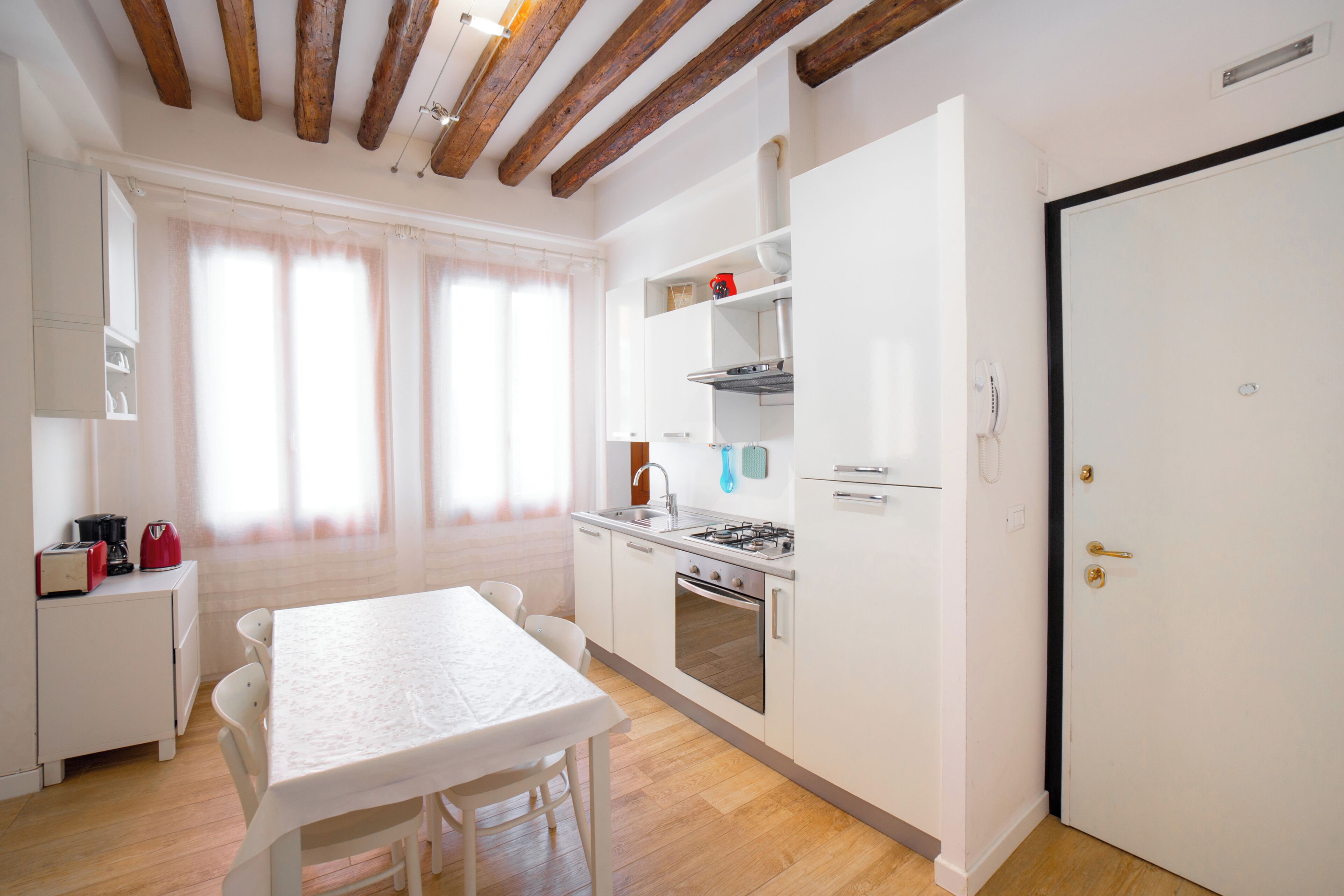 A modern kitchen with white cabinets, a dining table, and a large window with curtains.