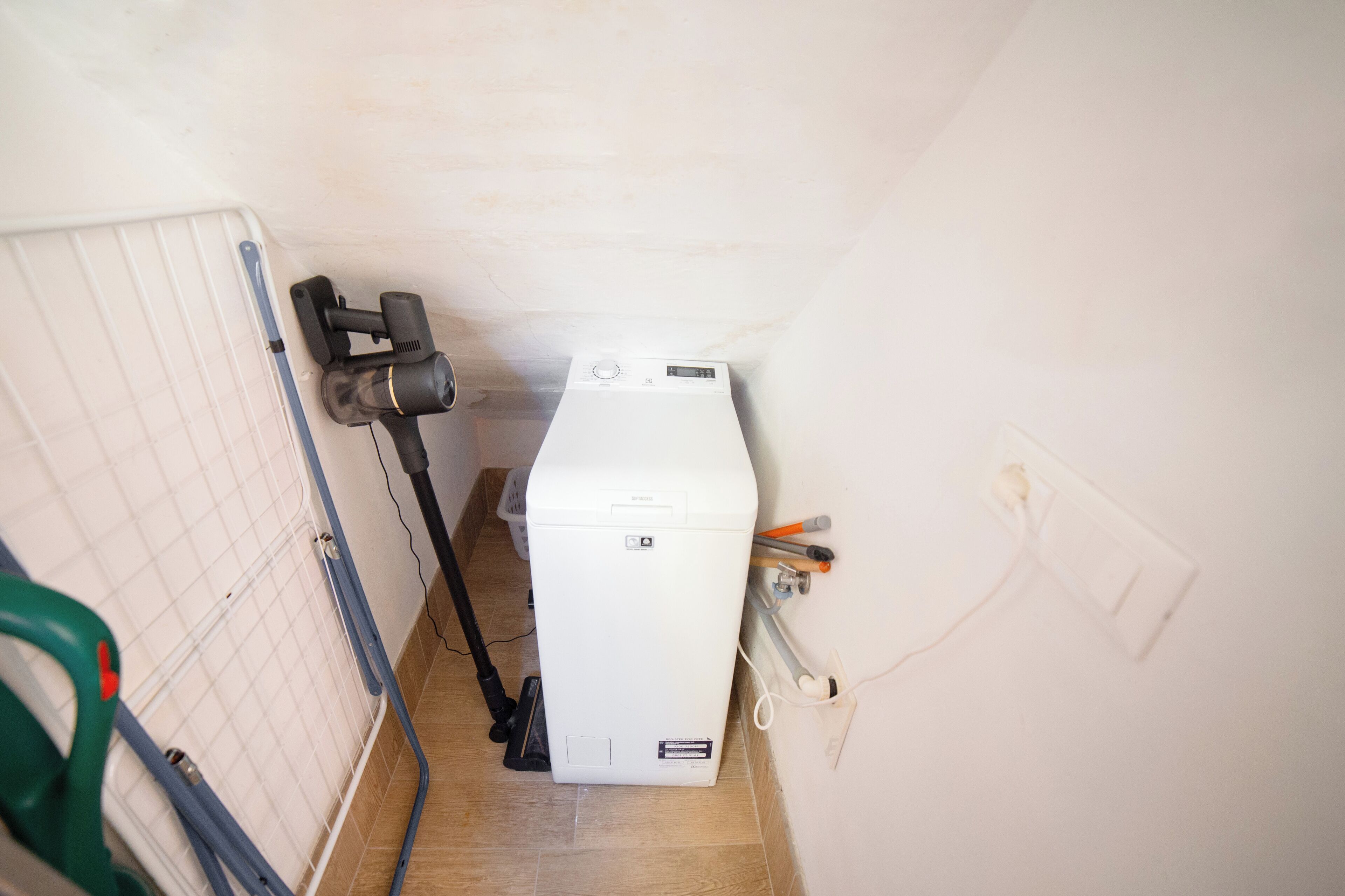 Een kleine kamer met een witte verwarming, een stofzuiger en een stofzuiger met een groene handgreep.