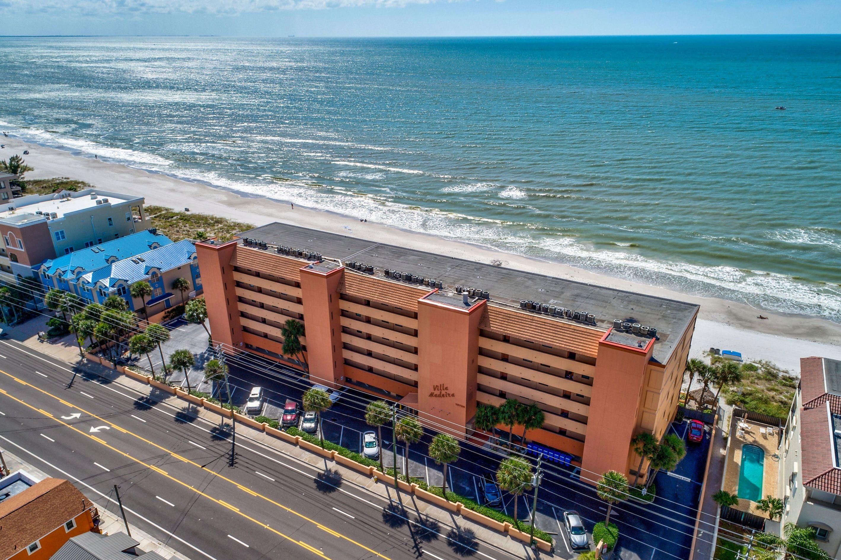 Un hotel sulla costa con parcheggio, vista sulla spiaggia e una strada trafficata.
