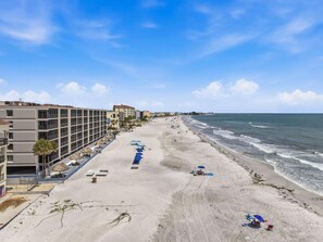 A beachside hotel with a long row of rooms, a sandy beach, and the ocean. - Villa Madeira 208 (Madeira Beach)