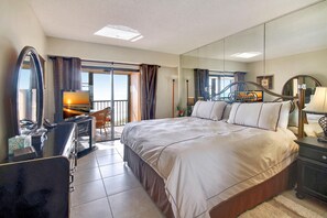 A hotel room with a large bed, a desk with a computer, a chair, a dresser, and a large mirror.