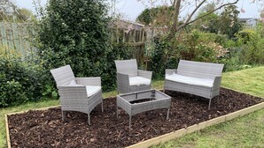 Un jardín con un macizo de madera elevado que contiene un sofá de mimbre y dos sillones.