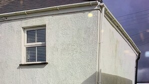 Un edificio blanco con una puerta numerada con el número 9, dos ventanas y un pequeño jardín con plantas en macetas.