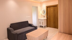 Una habitación moderna con un sofá de color oscuro, una mesa de centro de madera, un armario blanco con espejo y una puerta de madera.