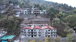 Un edificio de varios pisos con balcones, ubicado en una ladera rodeada de vegetación.