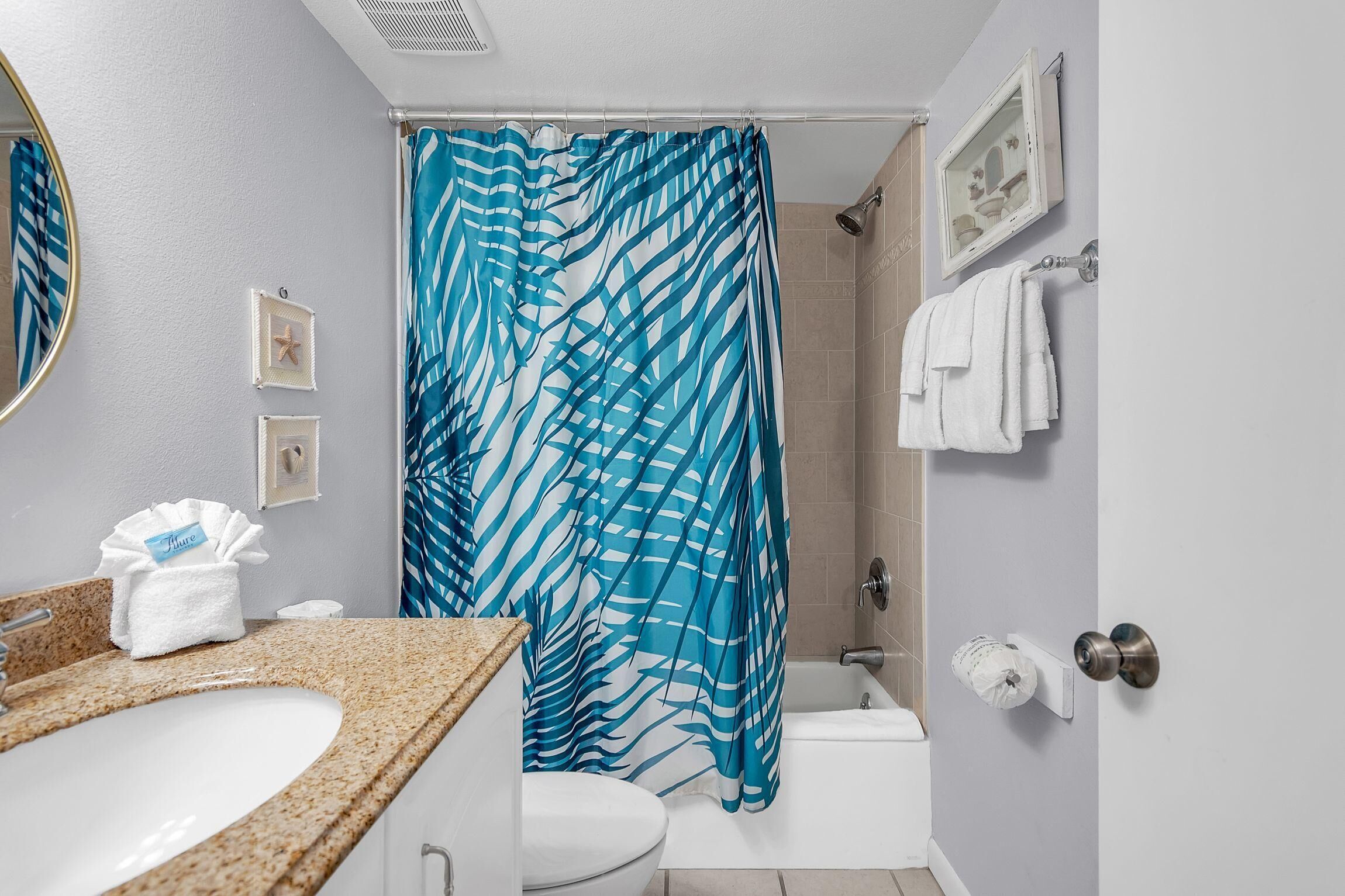 A bathroom with a white sink, a shower curtain with a blue leaf pattern, a toilet, and a towel rack with white towels.