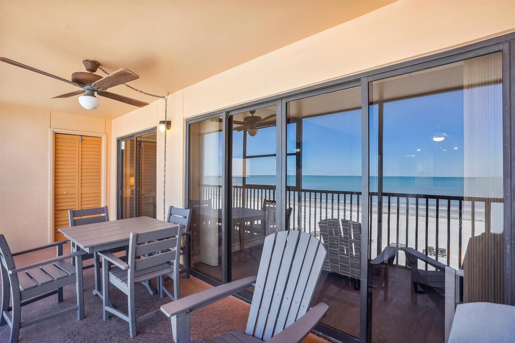 A balcony with a table and chairs, a ceiling fan, and a view of the beach.