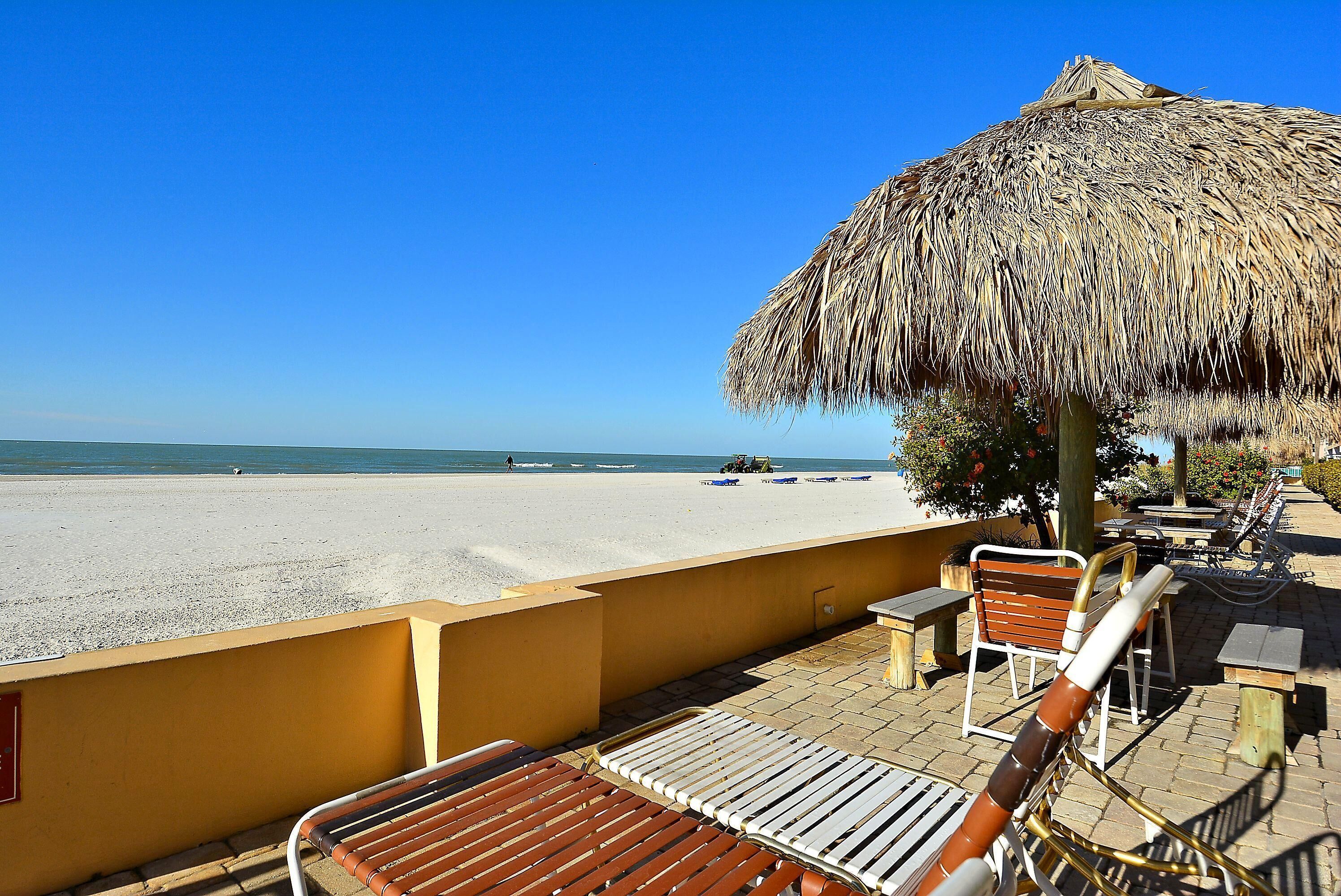A beachside terrace with wooden lounge chairs, a thatched umbrella, and a view of the beach and ocean.