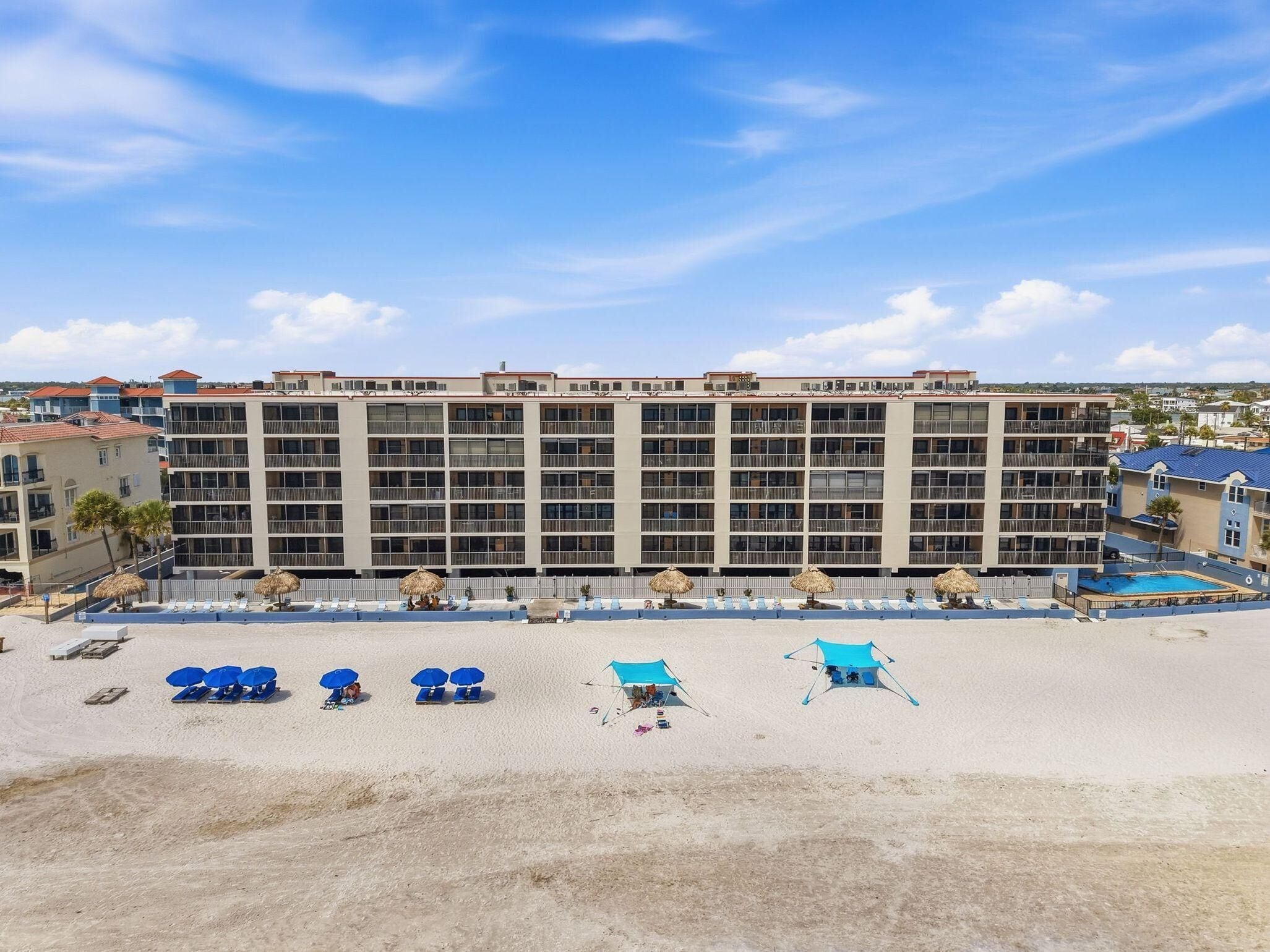A hotel with multiple balconies, a pool, and beach umbrellas.