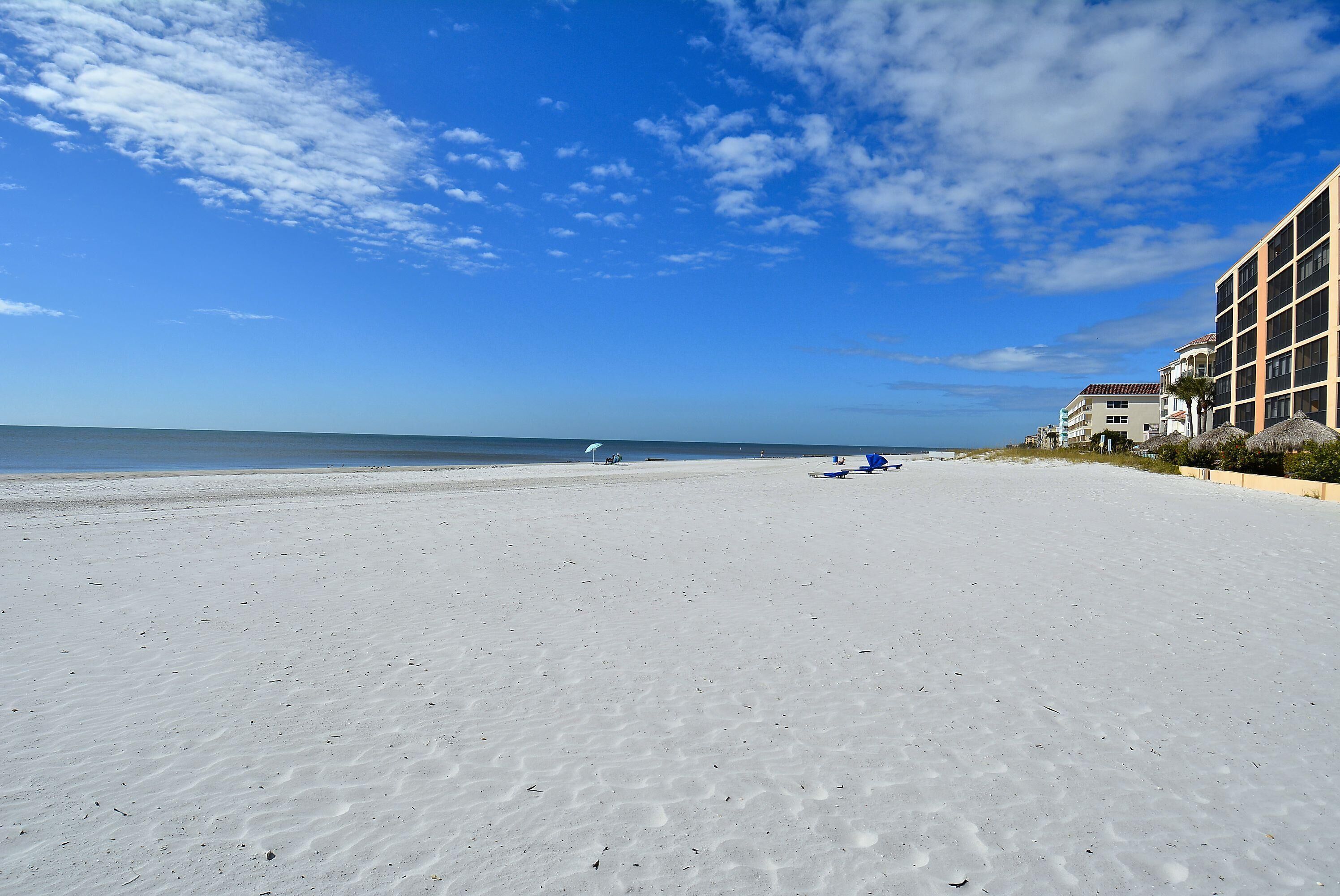 A beach with a clear sky, a few clouds, and a building on the right.