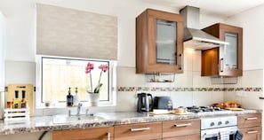 A modern kitchen with a granite countertop, wooden cabinets, a built-in oven, and a window with flowers.