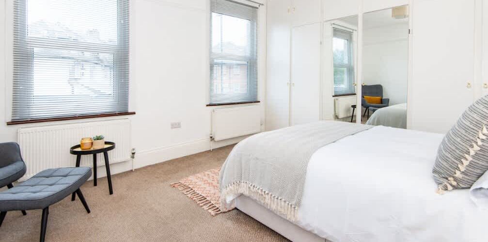 A bedroom with a bed, a chair, a small table, and a radiator.