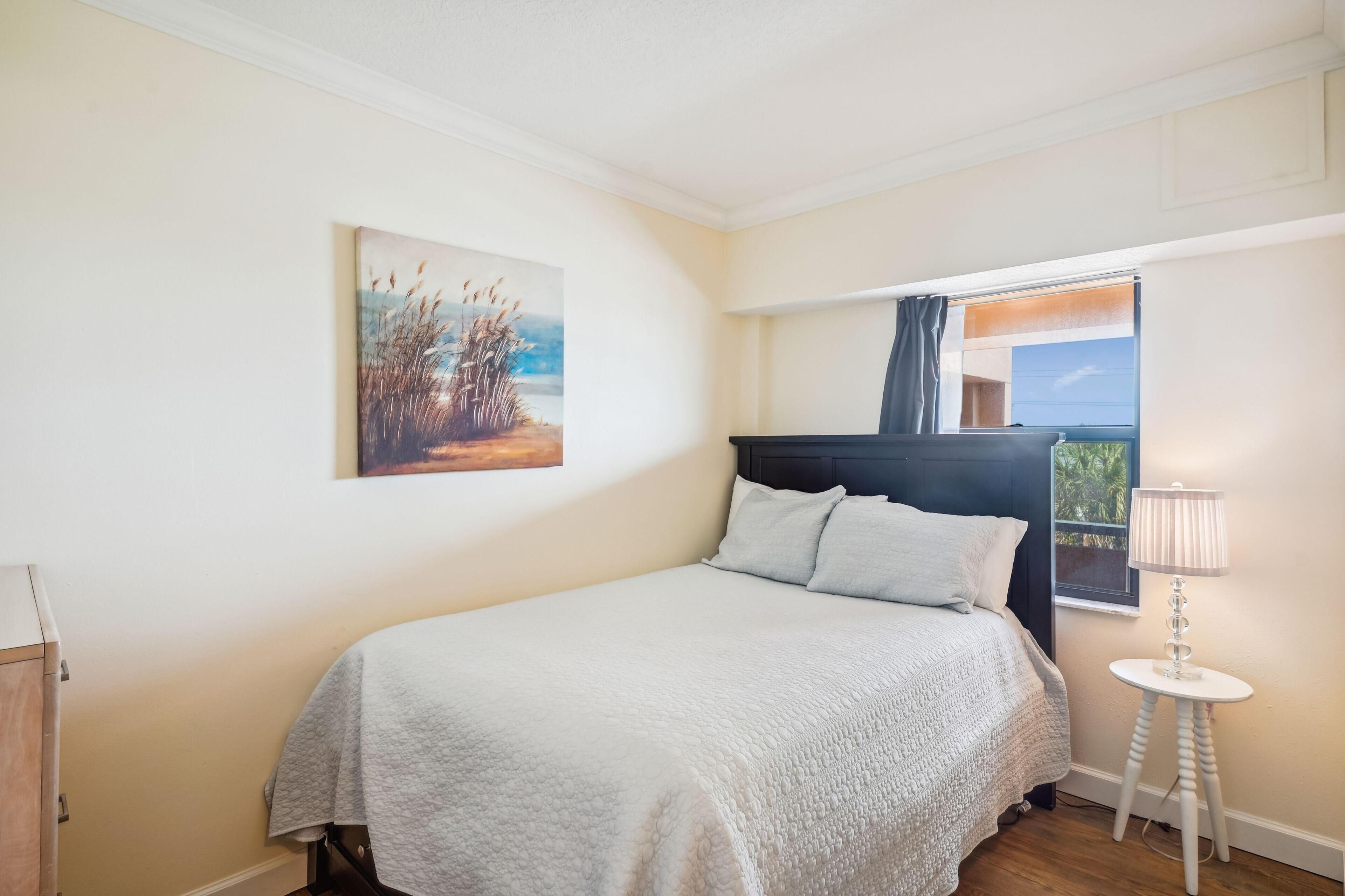 Une chambre à coucher avec un lit, une fenêtre avec des rideaux, une lampe et un tableau au mur.