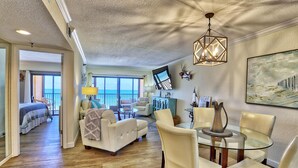 A spacious living area with a dining table and chairs, a sofa, and a view of the ocean through large windows. - Villa Madeira 406 (Madeira Beach)
