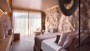 Un dormitorio moderno con una cama grande, una lámpara colgante redonda, una zona de estar con una mesita pequeña y un ventanal con cortinas de gasa.
