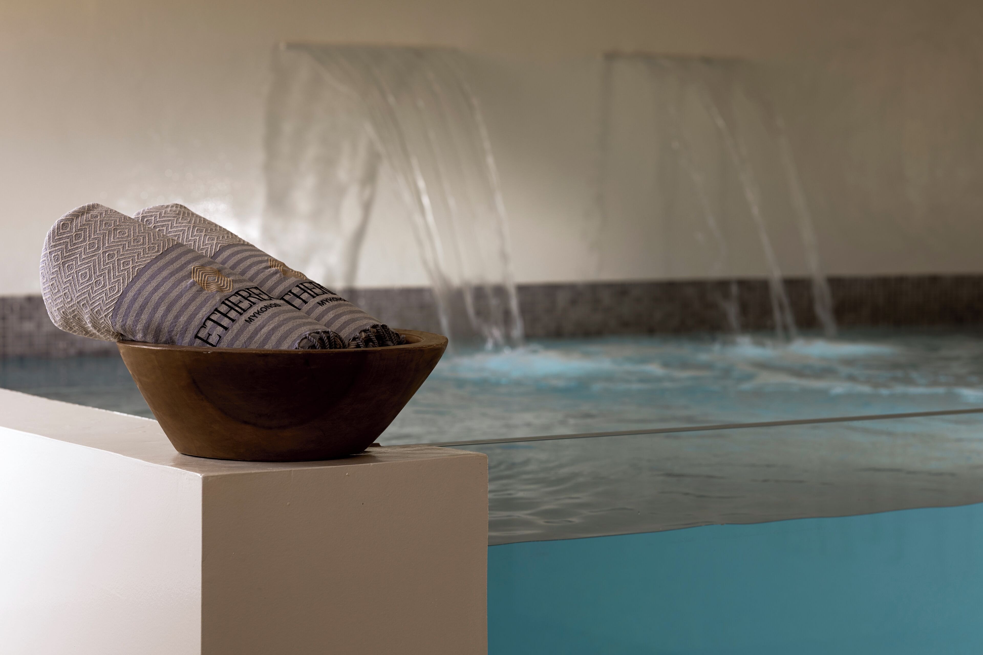 A wooden bowl with a towel on a ledge by a pool with a waterfall feature.