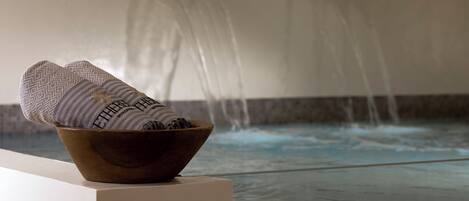 A wooden bowl with a towel on a ledge by a pool with a waterfall feature.