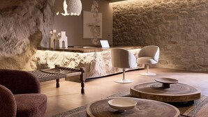 Un moderno espacio de spa con una pared de piedra, un mostrador de recepción, dos sillones y un banco de madera.