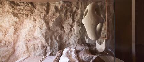 A bedroom with a stone wall, a bed with white linens, and a large abstract sculpture.