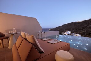A modern outdoor seating area with a pool, a table with glasses and a bottle, and a view of the coastline at dusk. - Ethereum Mykonos (Mykonos)