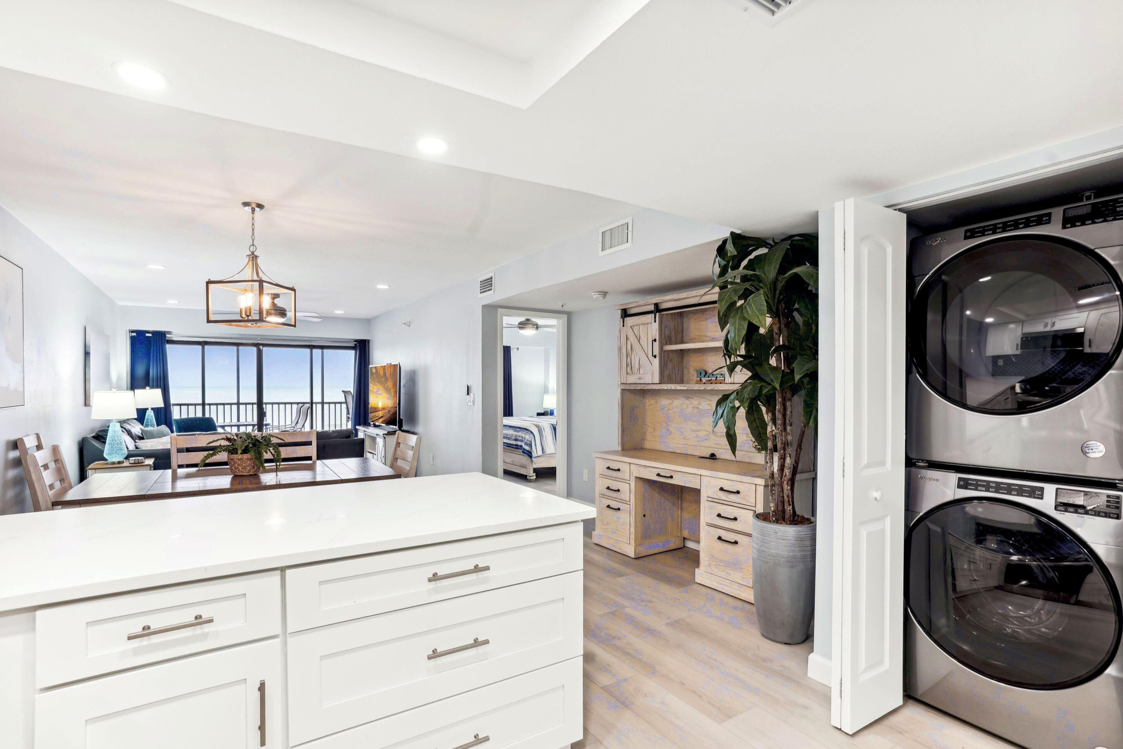 A modern laundry room with a large washing machine, a dryer, and a wooden desk.