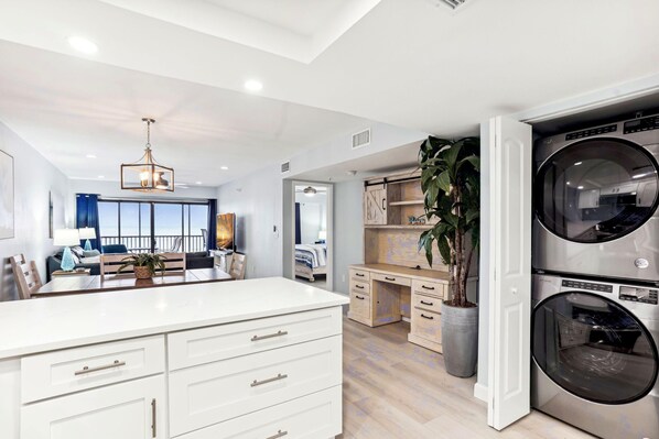 A modern laundry room with a large washing machine, a dryer, and a wooden desk.