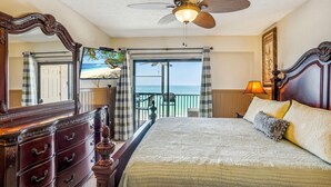A bedroom with a bed, a ceiling fan, a large mirror, a dresser, a balcony with a view of the sea, and a lamp. - Villa Madeira 504 - Premier (Madeira Beach)