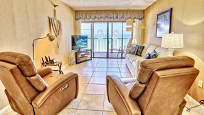 A living room with leather recliners, a television, and a view of the ocean through a sliding glass door.