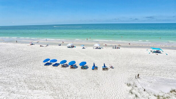 A wide sandy beach with several blue umbrellas and lounge chairs.