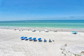 Une vaste plage de sable fin, parsemée de plusieurs parasols bleus et de chaises longues.